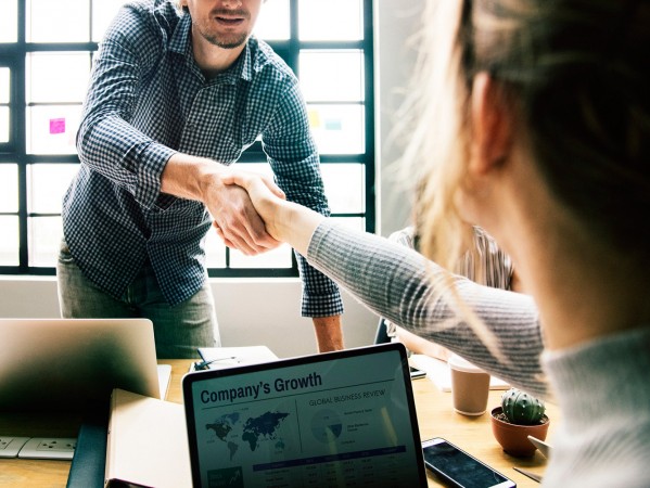 two people shake hands over their laptops on a table two people shake hands over their laptops on a table